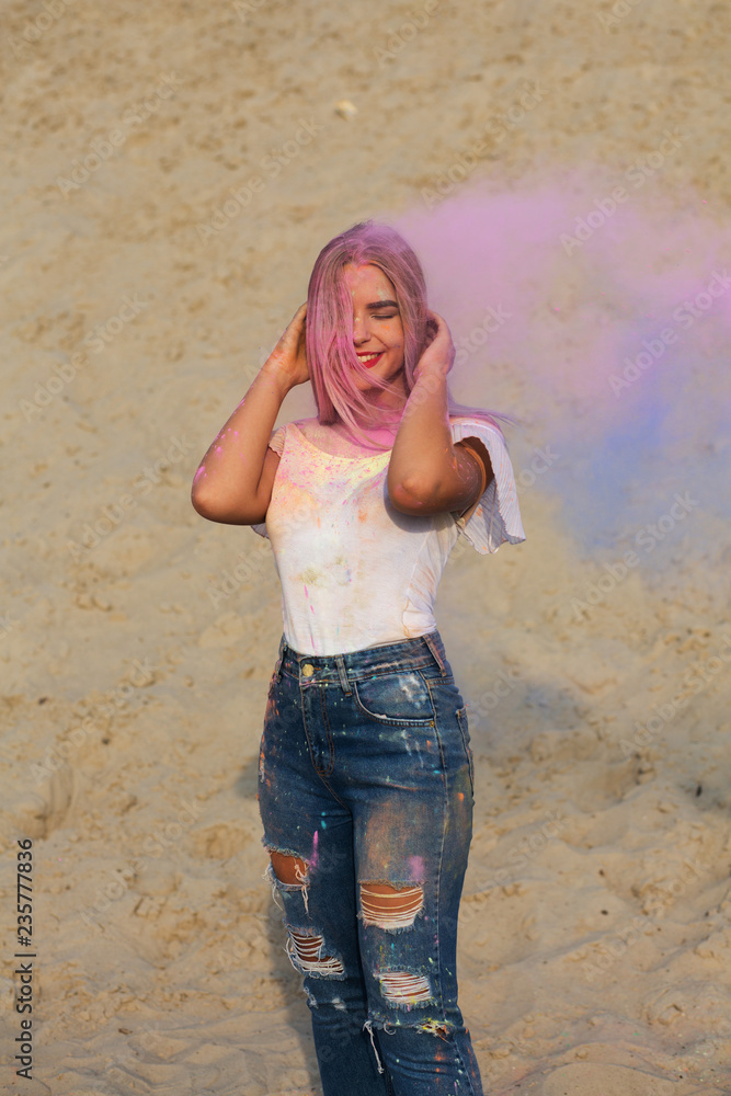 Cheerful blonde girl wearing white t shirt and jeans, playing with pink dry  Holi paint at the desert Stock Photo | Adobe Stock