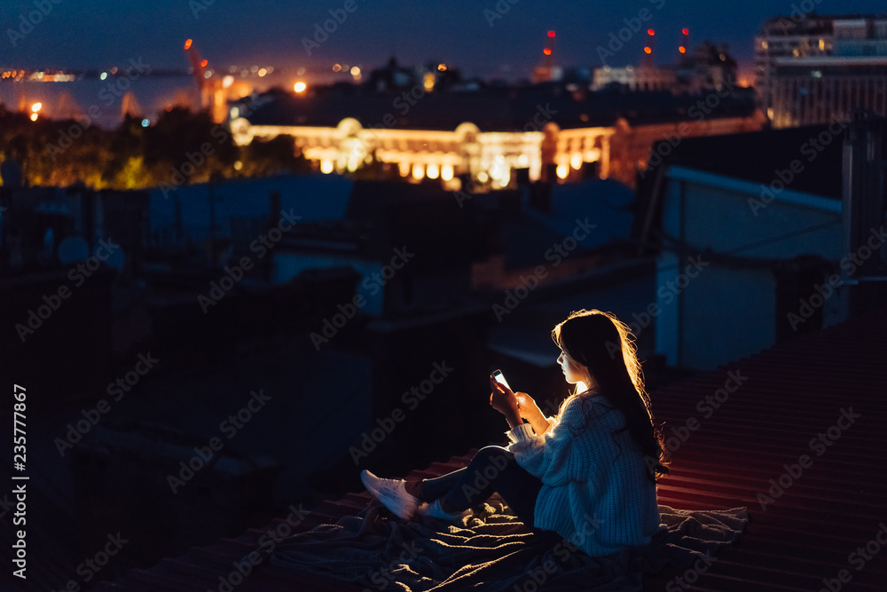 Young girl sits at night on the roof of a house. Beautiful evening