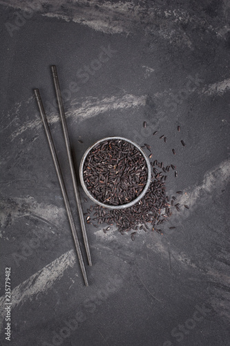 Top view of uncooked black rice in gray bowl with wooden chinese chopsticks
