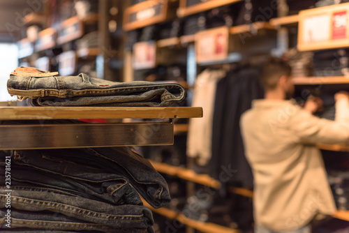 Selective focus, shallow dof image of clothes shop with trendy clothing on hanger and blurry customer shopping, selecting textile product in background.