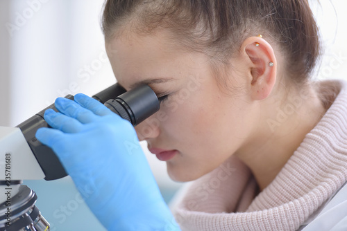 Young female male scientist looking through a microscope in a laboratory doing research, microbiological analysis, medicine.