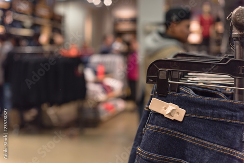 Selective focus, shallow dof image of clothes shop with trendy clothing on hanger and blurry customer shopping, selecting textile product in background. © trongnguyen