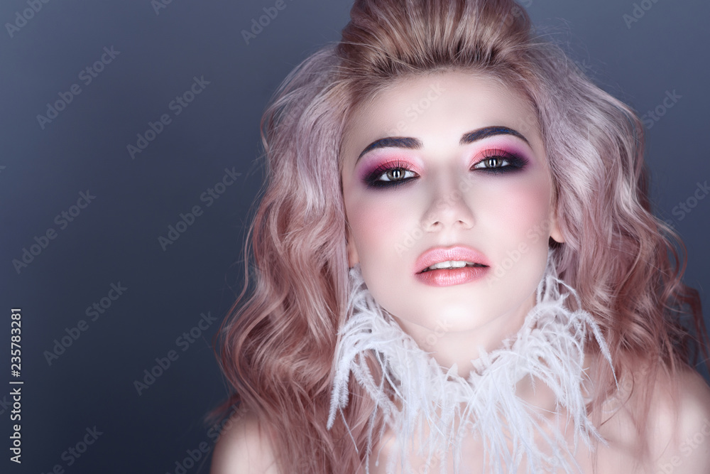 Closeup portrait of beautiful young model with creative colorful make up and wavy hairstyle wearing stylish white feather collar. Isolated on grey background. Text space. Studio shot.