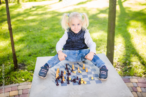 Funny Caucasian baby girl blonde does not want learn, does not want to school, want to play, laugh and indulge. child with hair ponytail sits table legs forward, spread out, mess, tabletop logic game photo