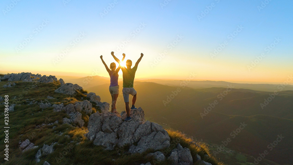 DRONE: Flying over sporty couple outstretching arms after a successful hike.