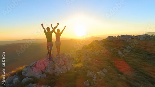 LENS FLARE  Caucasian couple celebrates reaching top of mountain at sunset.