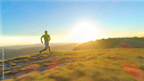 LENS FLARE: Athletic young man sprints down a grassy hill on a sunny morning