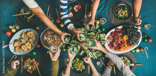 Company of friends or family gathering for Christmas or New Year party dinner at festive table. Flat-lay of human hands holding glasses with drinks, feasting and celebrating holiday together, top view