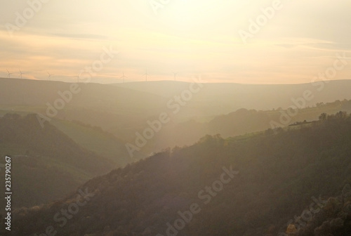 a soft hillside tree covered valley landscape blurred by fog at sunset glowing a warm orange color