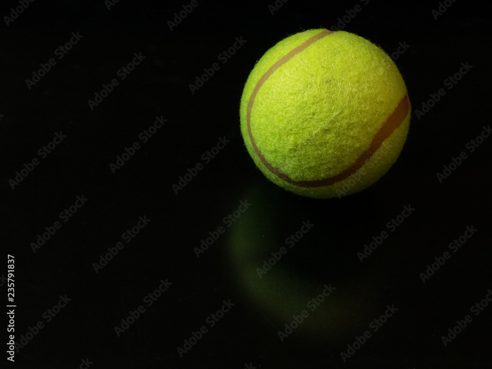 one yellow green tennis ball on dark glossy surface