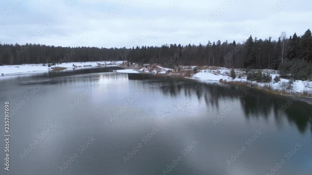 Aerial view. The lake in the winter forest. Flying over a not frozen lake in cloudy winter weather. Colorful landscape, frosty evening. Winter Russian nature. Lake surrounded by snow. 4K Aerial view. The lake in the winter forest. Flying over a not frozen lake in cloudy winter weather. Colorful landscape, frosty evening. Winter Russian nature. Lake surrounded by snow. 4K