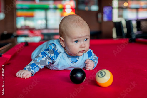 little boy laying on red billiard table with two balls (black and yellow)
