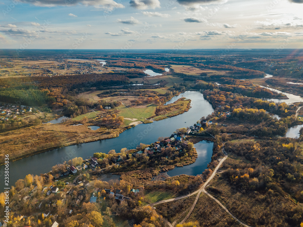 Aerial view of rural landscape in autumn. Small village houses, river, autumn trees, farm fields from drone point of view