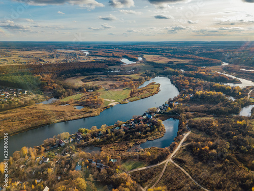 Aerial view of rural landscape in autumn. Small village houses, river, autumn trees, farm fields from drone point of view