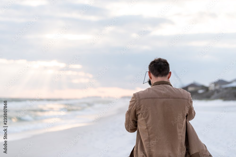 Dramatic sunset with sun god rays beams in Santa Rosa Beach, Florida with back of young man photographer standing looking at coastline coast