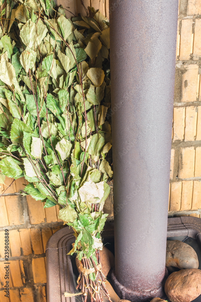 Green birch broom on the stove near the pipe in the bathhouse Green birch broom on the stove near the pipe in the bathhouse