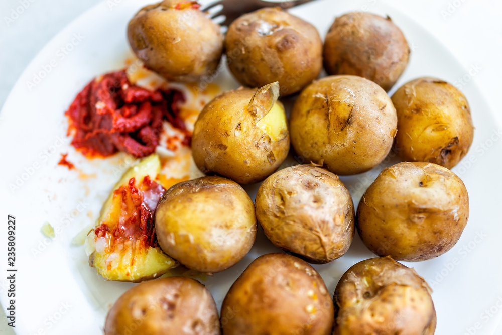 Closeup flat table top view of fresh boiled steamed baked small potatoes on white plate with tomato paste ketchup, fork, many tubers Closeup flat table top view of fresh boiled steamed baked small potatoes on white plate with tomato paste ketchup, fork, many tubers