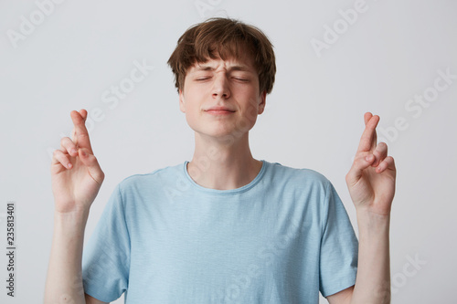 Fotografie Positive faithful young guy, closing eyes with hope, crossing fingers while maki