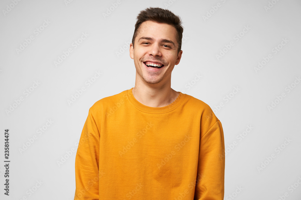 Cheerful positive male youngster, dressed casually, glad to spend time with friends, joking laughing, has a good time. Positive emotions and feelings, isolated over white background - obrazy, fototapety, plakaty 