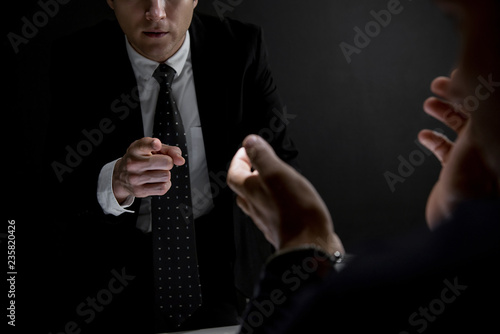 Detective pointing hand to criminal man in dark interrogation room
