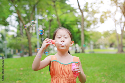 Asian little girl blowing soap bubbles in green park