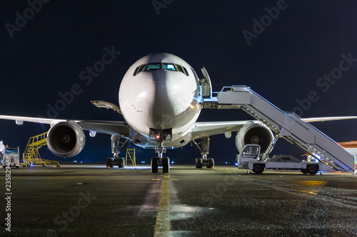 Front view of white wide-body passenger airplane with a boarding steps at the night airport apron