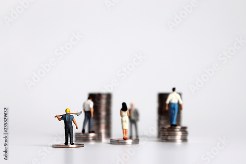 Miniature people with piles of coins. The concept of economic inequality between employers and workers.