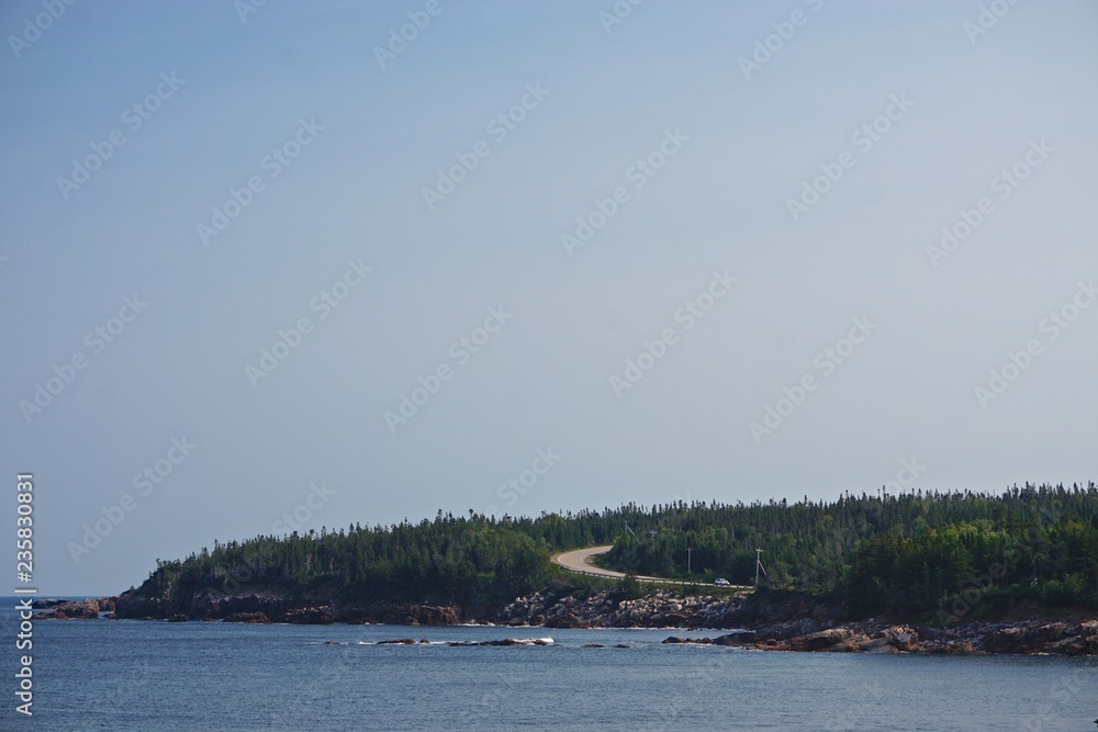 Black Brook Beach, Cape Breton, Nova Scotia, Canada: View of a winding road through a pine forest under a clear blue sky.