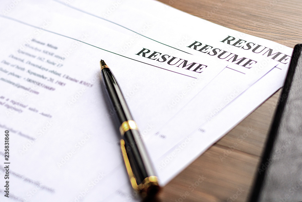 Resume (curriculum vitae, cv) and pen on a written wooden table.