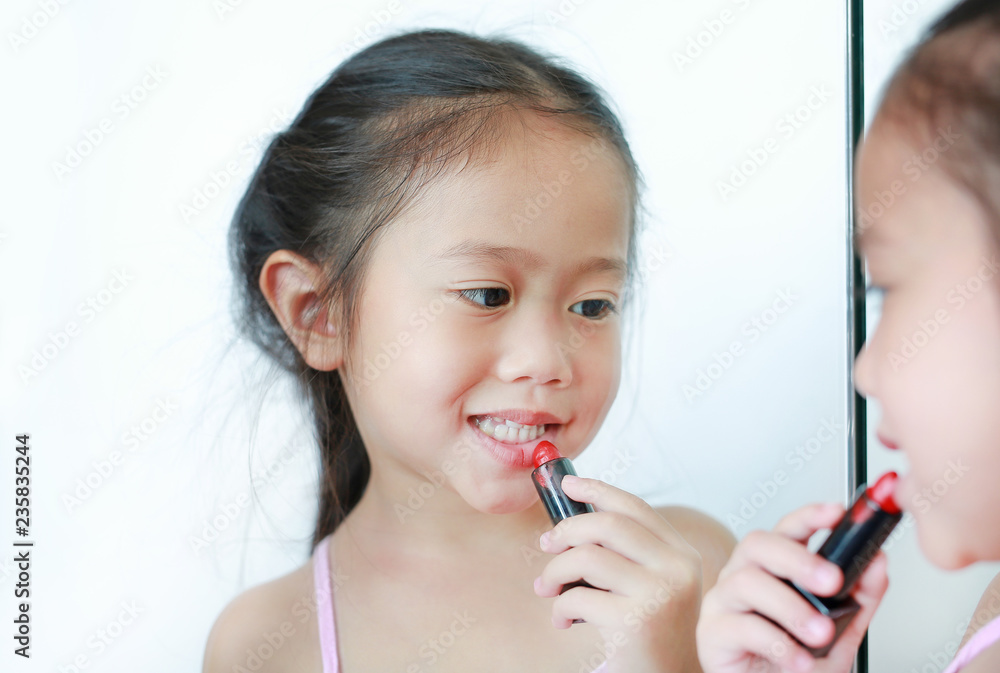 Cute little Asian child girl trying lip gloss near a mirror.
Cute little Asian child girl trying lip gloss near a mirror.