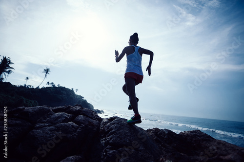 Woman trail runner running at rocky mountain top on seaside