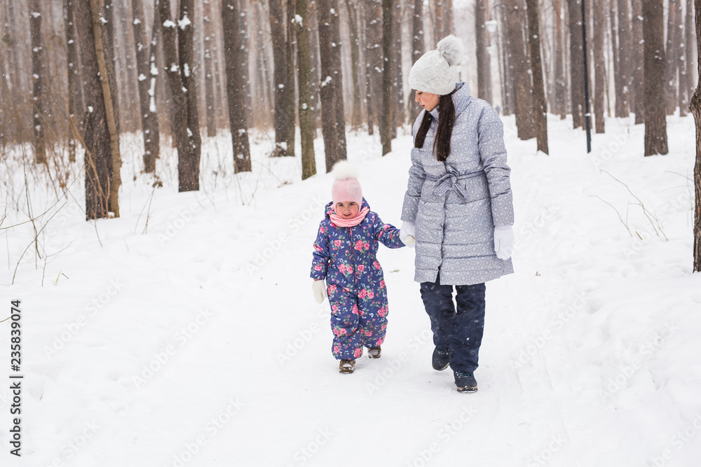 Family, winter and nature concept - Young cheerful mother with cute little daughter walking in the snow park