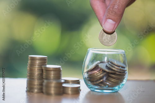 Woman's hand putting coin into glass of bottle for saving money, Saving money concept