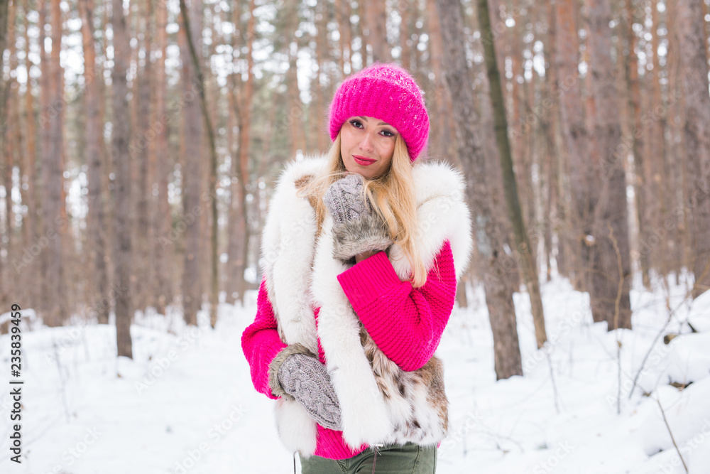 Beauty, nature and people concept - beautiful blond woman walking in pink hat and sweaters in winter wood and smiling Beauty, nature and people concept - beautiful blond woman walking in pink hat and sweaters in winter wood and smiling