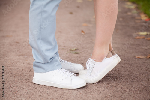 Loving woman standing tiptoe, trying kiss boyfriend outdoors in park, couple in love in jeans and white sneakers embracing, hugging on street, small girlfriend and tall man, romance moment close up
