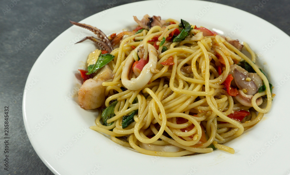 Spaghetti seafood in a white dish on a black stone floor table.