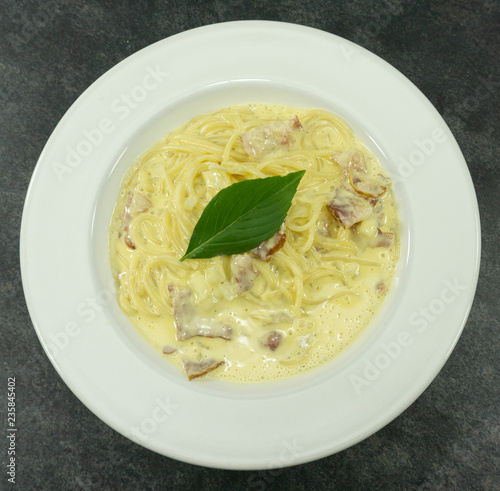 Spaghetti Carbonara in a white plate with Bacon and milk line yellow on a stone floor table,Top view, Copy space Close up.. photo