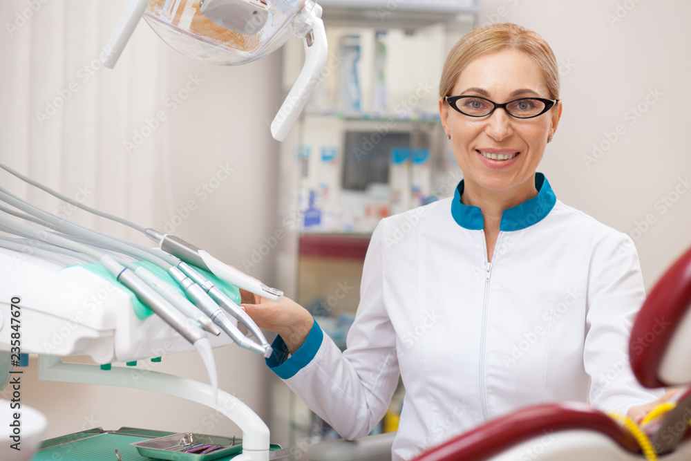 Happy mature female dentist at work. Cheerful professional dentist adjusting dental lam, preparing for dental examination with patient, copy space. Professionalism, experience concept Happy mature female dentist at work. Cheerful professional dentist adjusting dental lam, preparing for dental examination with patient, copy space. Professionalism, experience concept