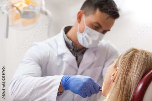 Professional dentist working at his office  examining teeth of a female patient. Male dentist in lab coat and medical mask checking teeth of a woman  copy space. Professionalism  experience concept