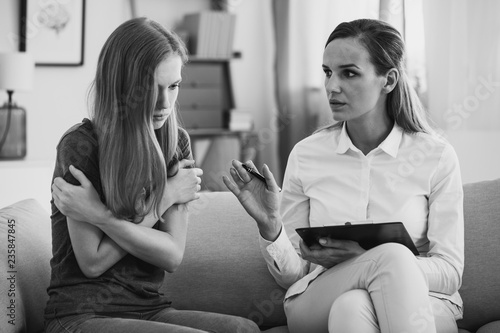 Fotografie Black and white photo of professional pedagogue relieving stress of young teenage girl during psychotherapy
