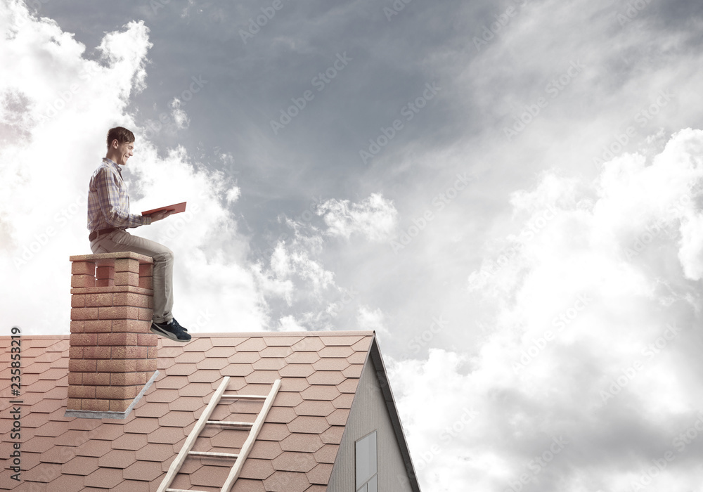 Handsome man on brick roof against cloud scape reading book Handsome man on brick roof against cloud scape reading book