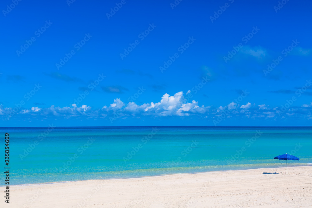 Blue beach umbrella parasol on the tropical beach. Vacation background. Idyllic beach landscape.