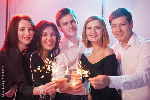 New year party, celebration and holidays concept - Young cheerful men and women holding burning sparklers
