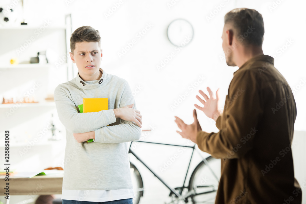 Fototapeta premium irritated father gesturing and looking at teen son at home