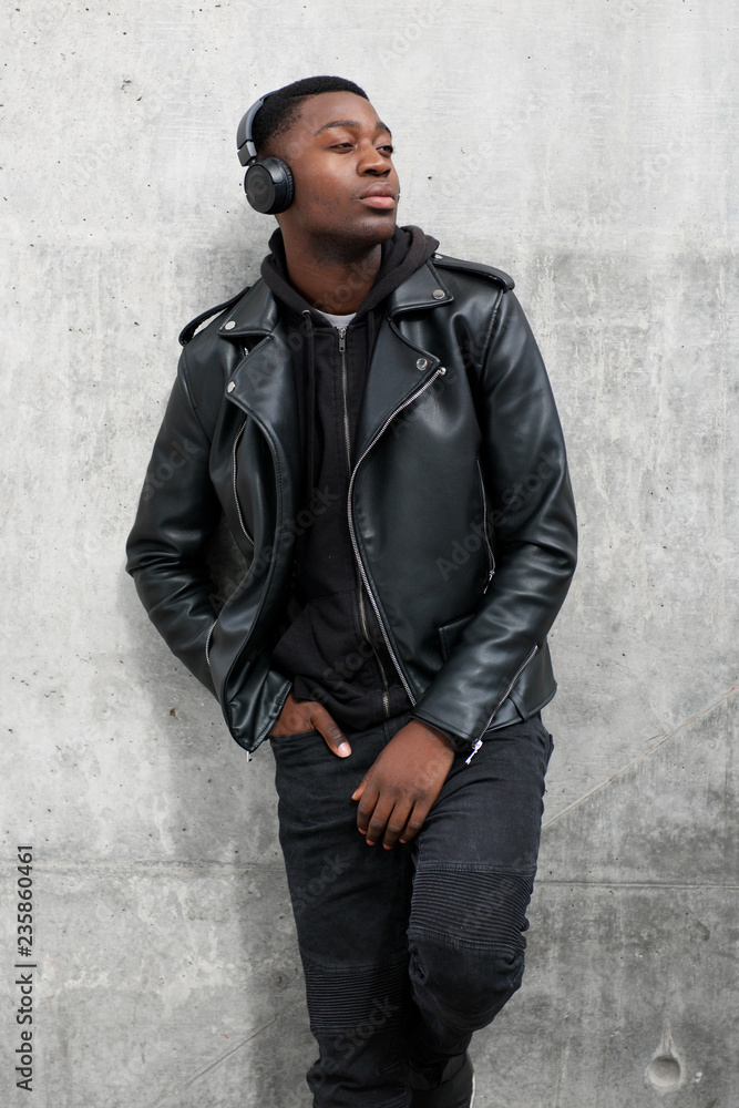 cool young black man in leather jacket listening to music with headphones