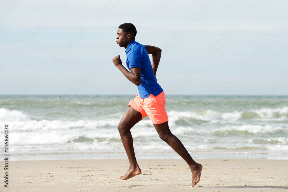 healthy african american man running barefoot at beach healthy african american man running barefoot at beach