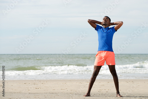 Full body portrait of young african american man relaxing at beach with hands behind head