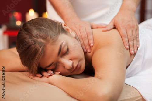 Relaxed young woman enjoying soothing massage in the hands of skilled masseur. Spa therapist working with his female client, massaging her back at beauty center. Serenity, harmony, enjoyment concept