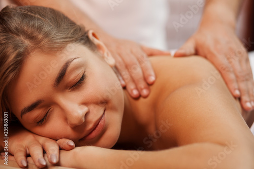 Cropped close up of a beautiful happy healthy young woman smiling with her eyes closed  while professional masseur massaging her back and shoulder  copy space. Medical treatment  stress relief concept