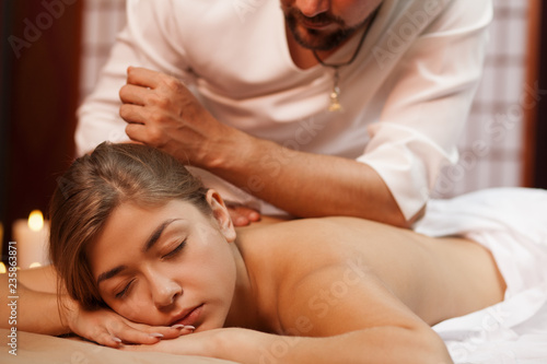 Professional spa therapist giving relaxing back massage to his female client. Beautiful woman enjoying traditional massage therapy at spa center. Attractive woman relaxing at beauty clinic